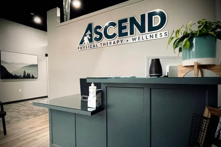 The front desk and Ascend Physical Therapy + Wellness wall sign in the clinic lobby
