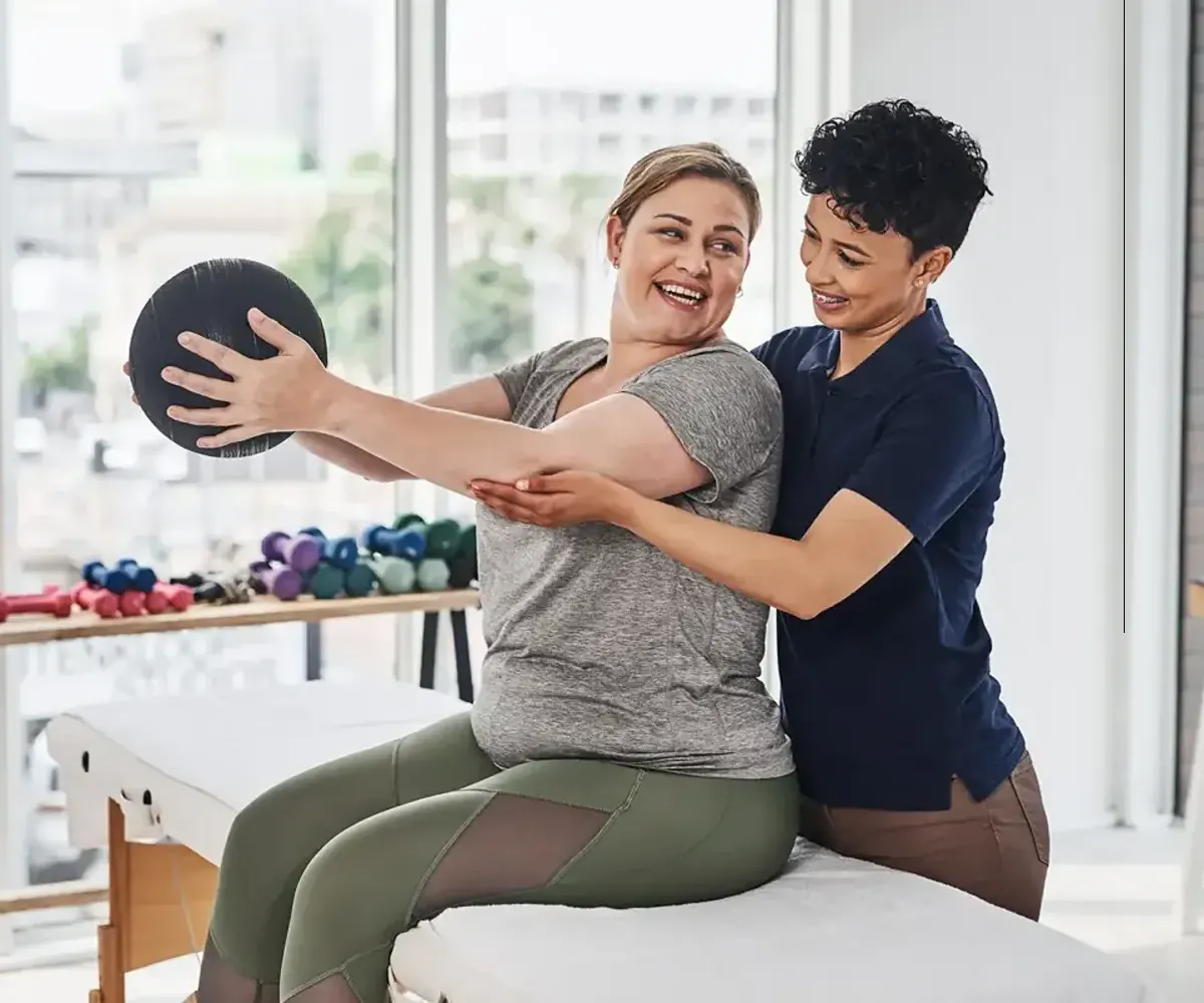 Physical therapist helping a smiling patient with a medicine ball exercise